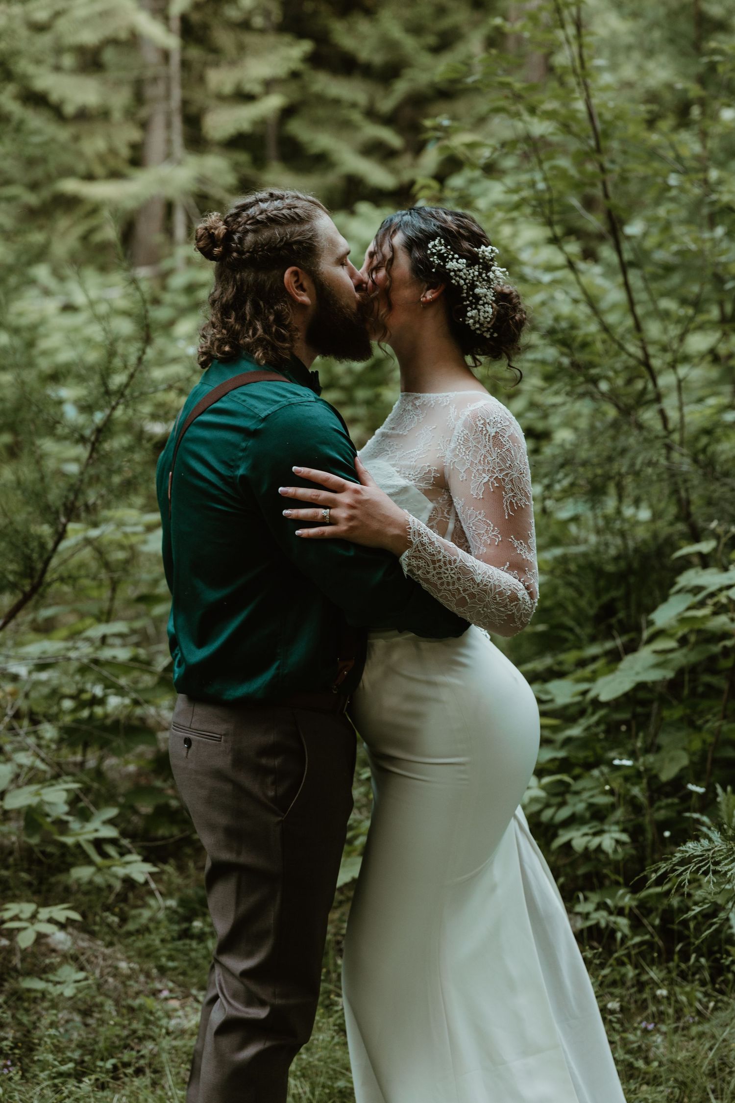 A tender kiss shared between newlyweds in a lush green forest setting.