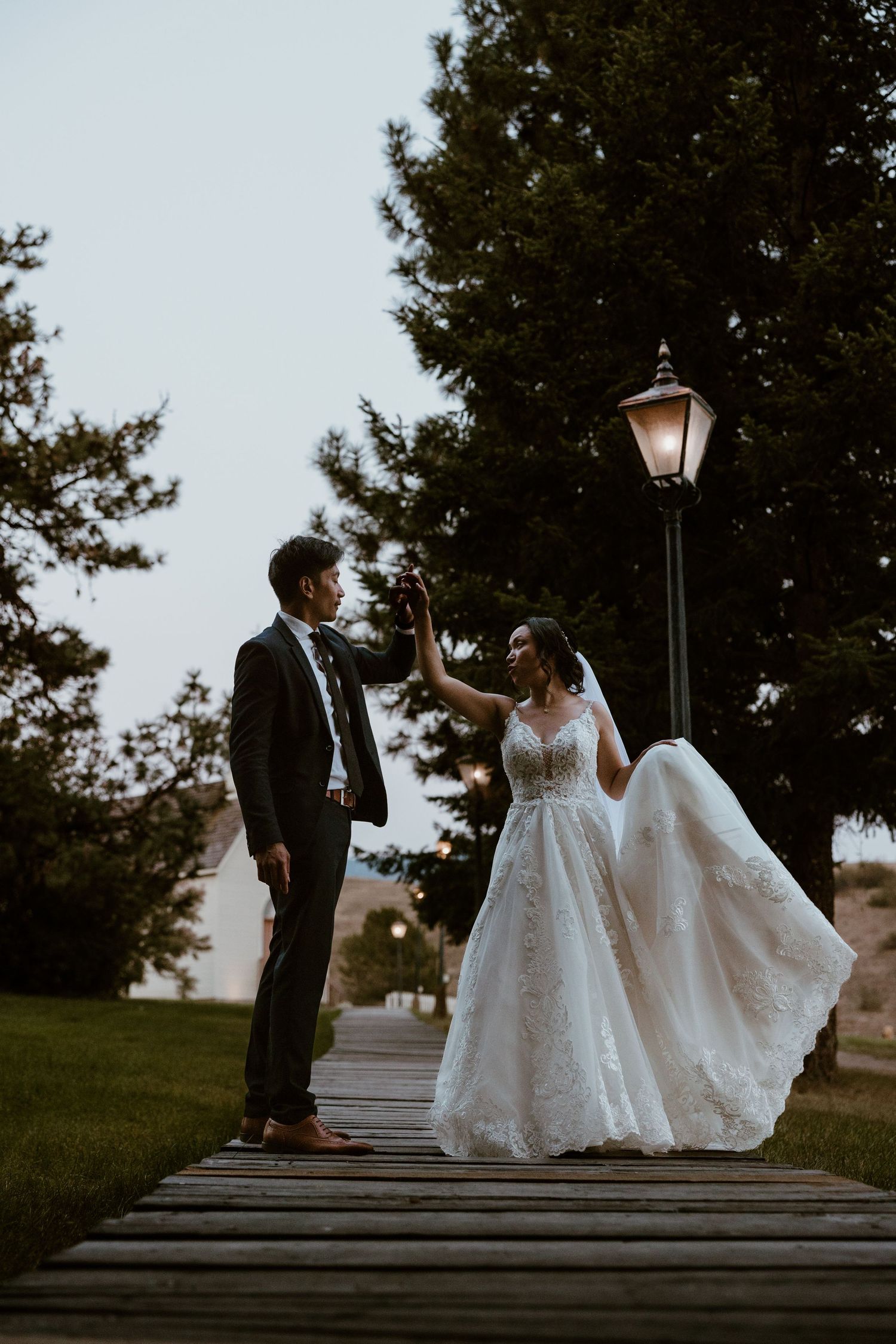 Couple shares romantic moment on wooden boardwalk at dusk near vintage lamppost.