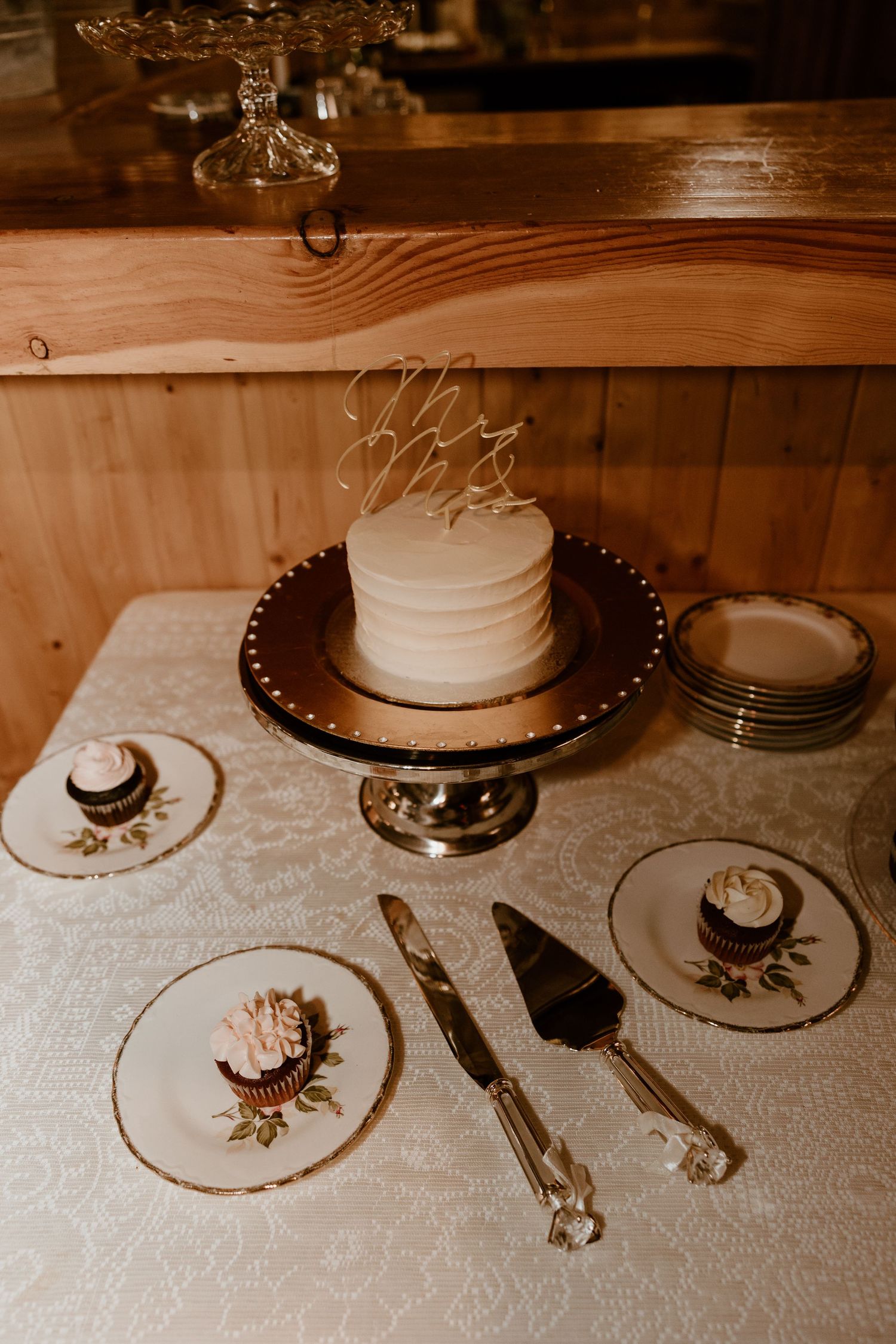 Wedding cake and place settings displayed on rustic wooden table.