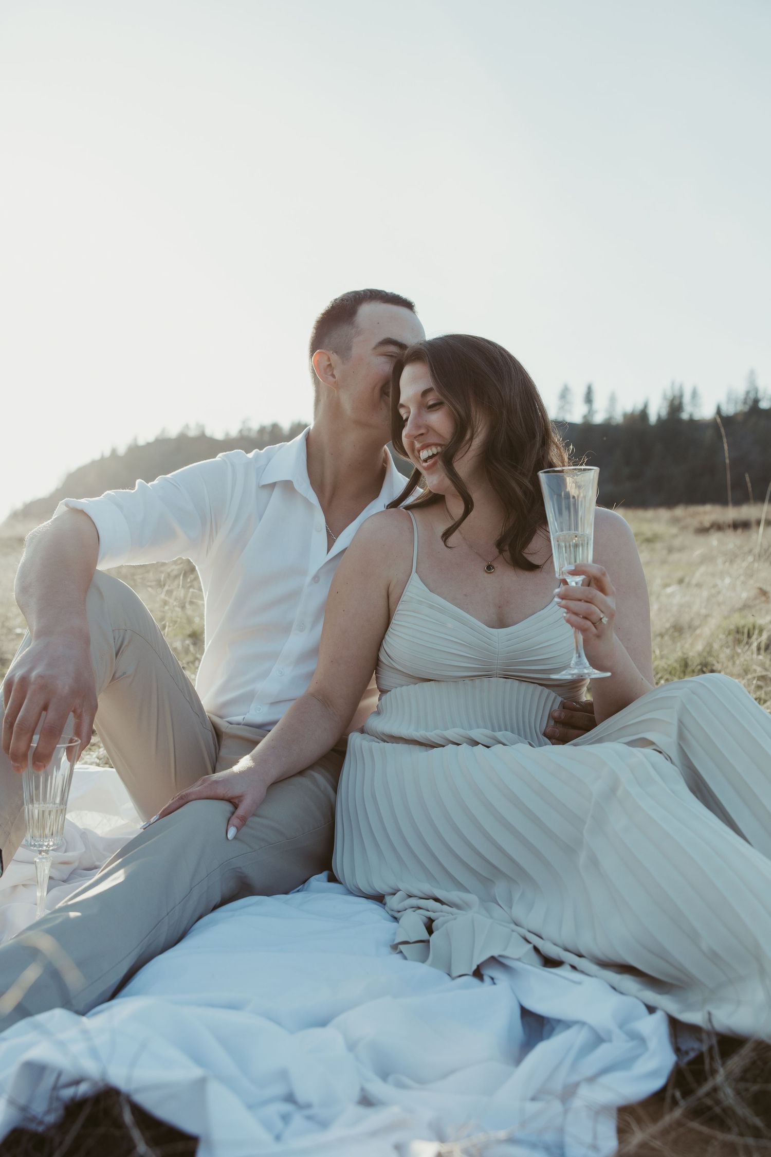 A couple enjoys champagne during a romantic sunset picnic in formal attire.