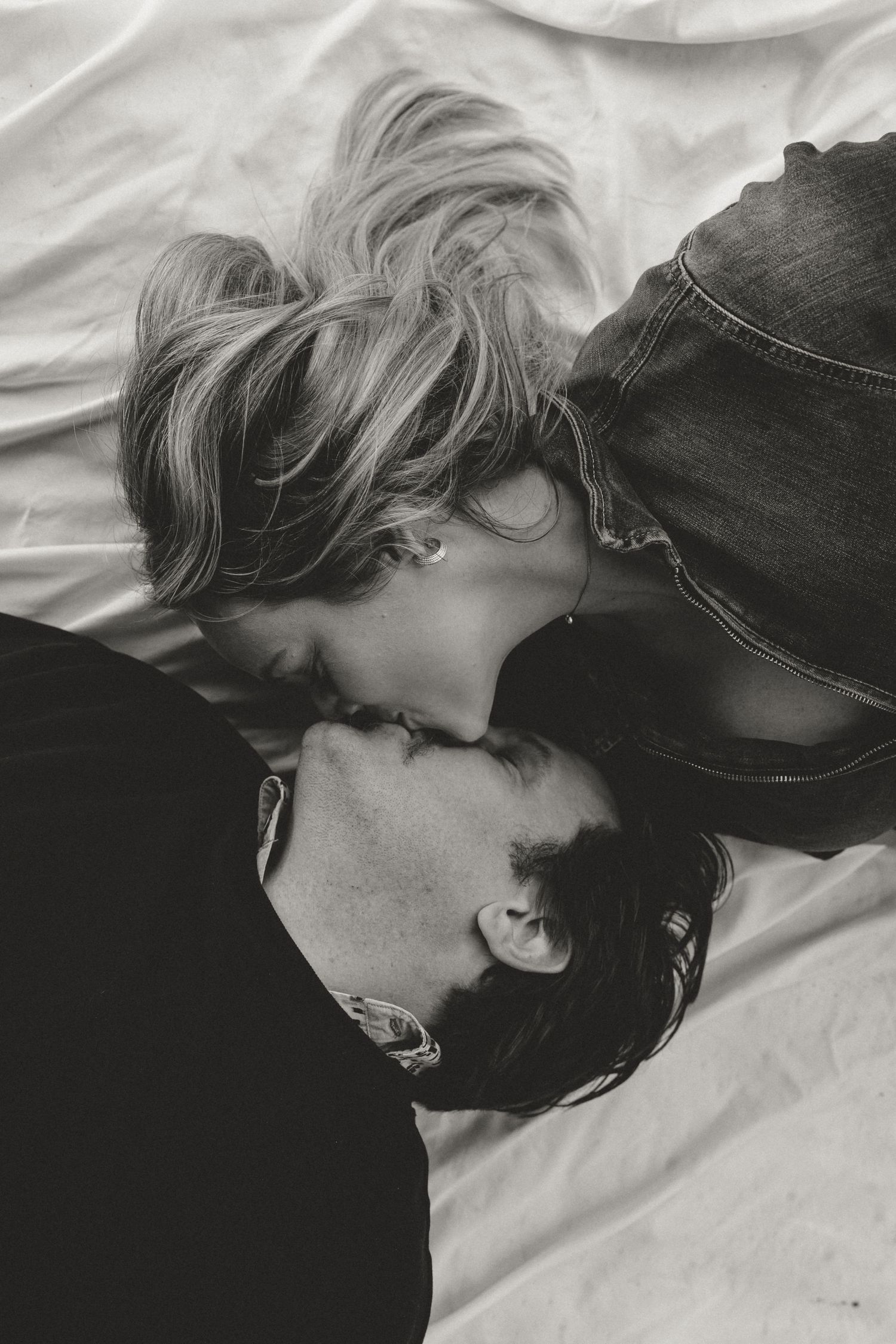 An intimate black and white portrait of a couple sharing a tender moment on white sheets.