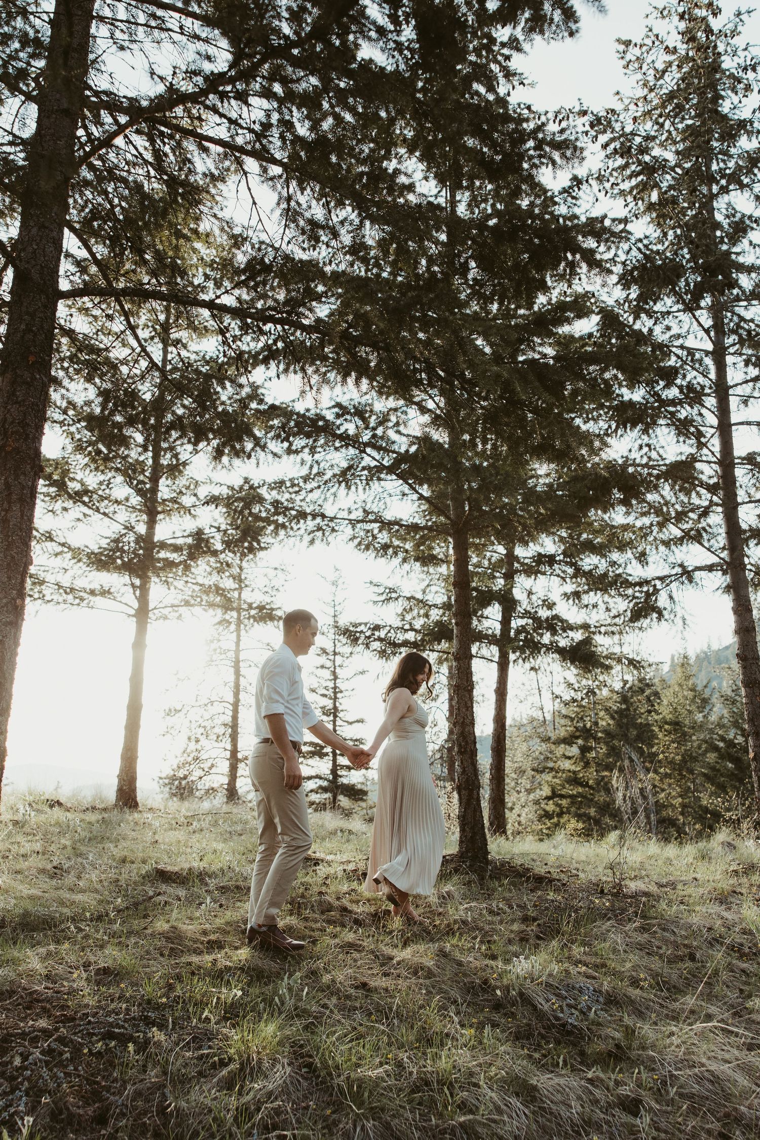 A couple shares an intimate moment among tall pine trees during a sunset photoshoot in nature.