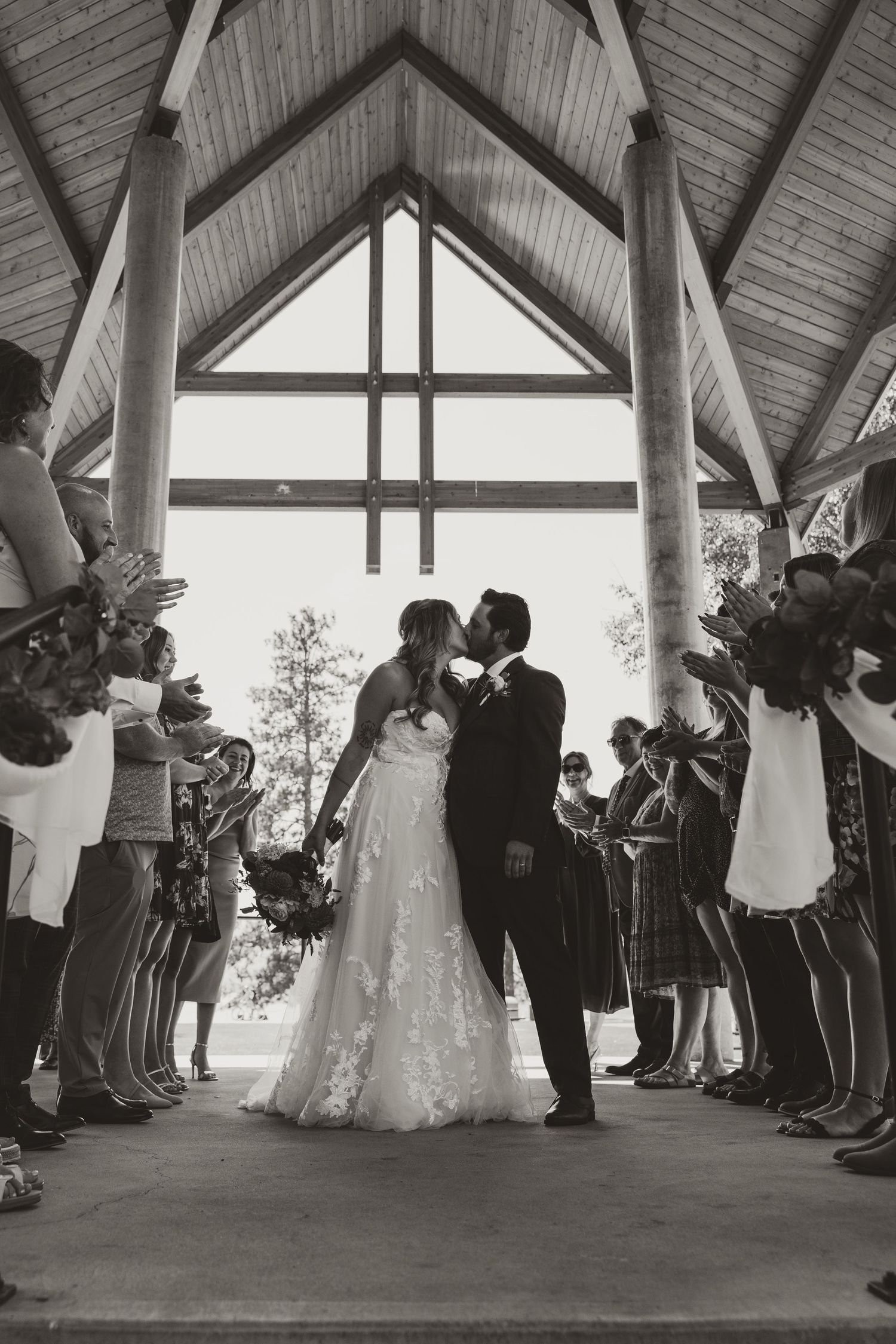 Wedding ceremony in a chapel with a couple kissing under vaulted wooden beams.