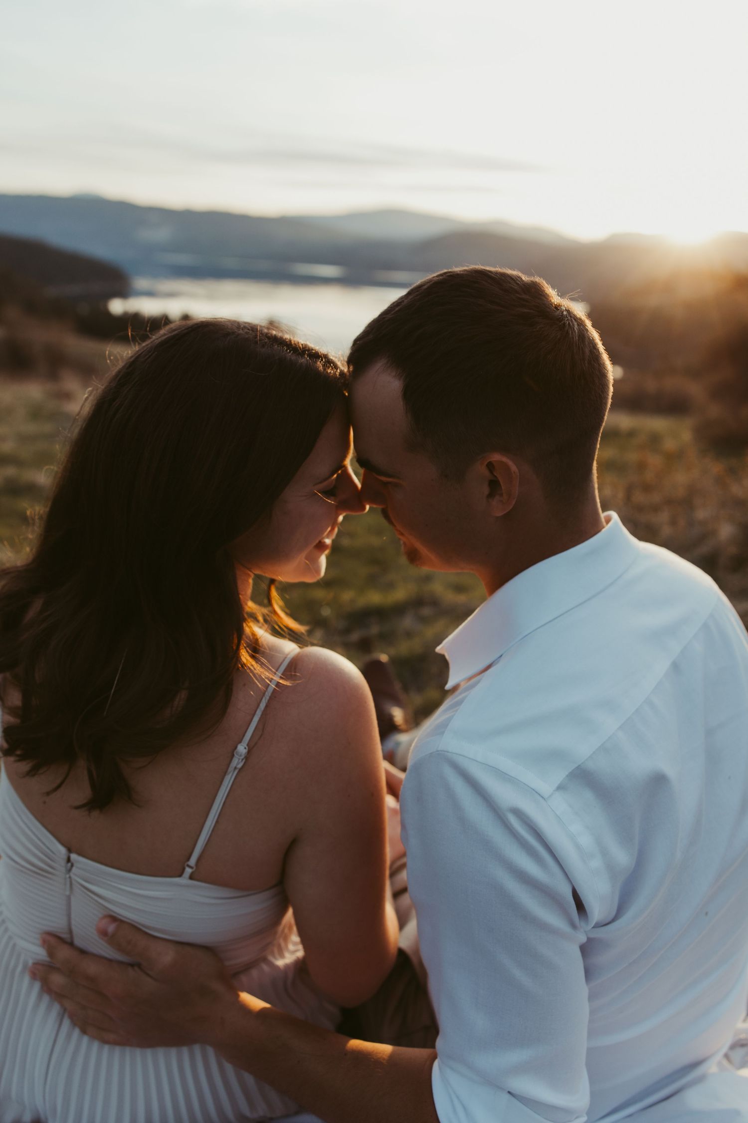 An intimate portrait of a couple sharing a close moment during sunset with mountains in the background.