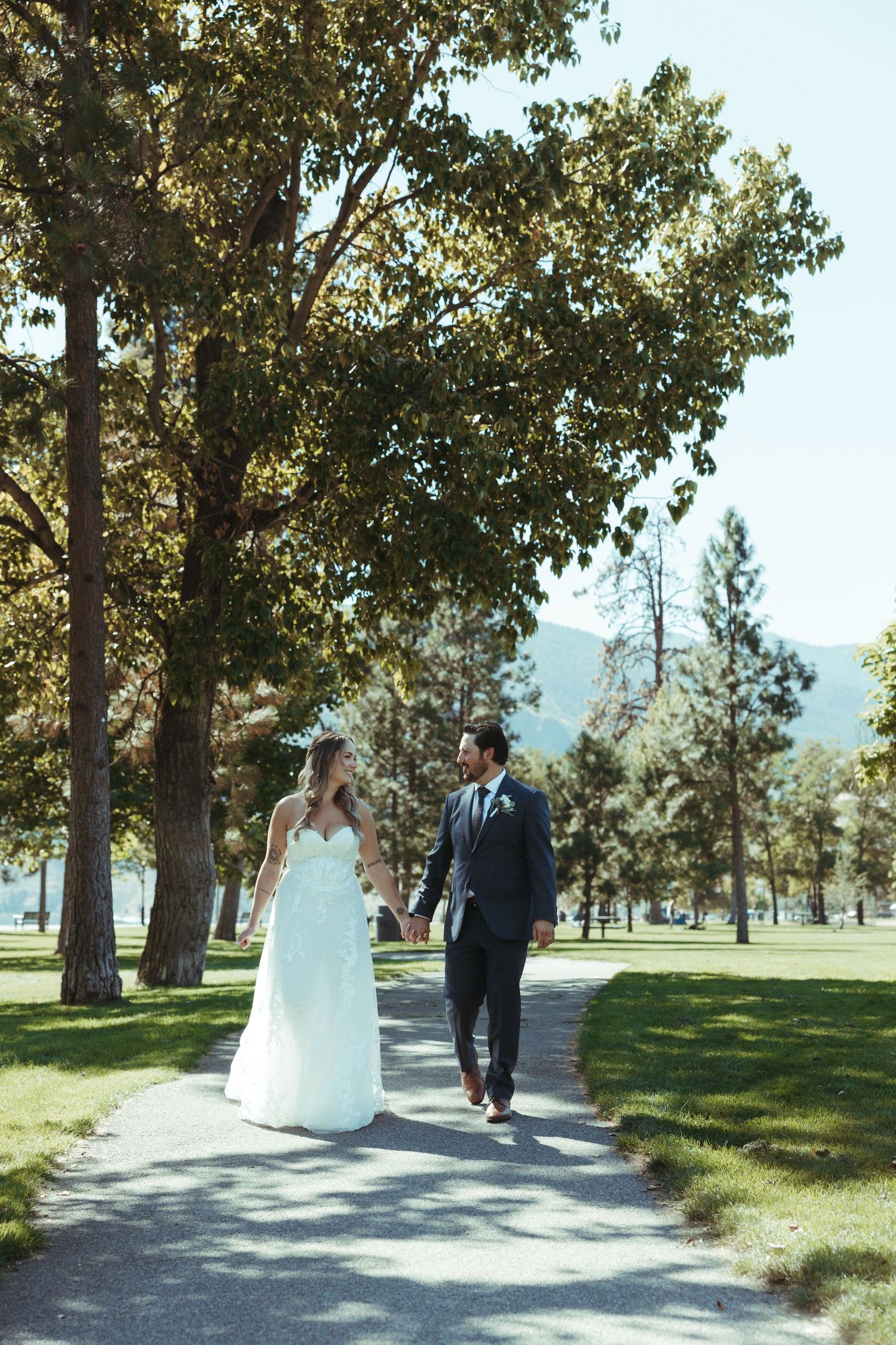 Bride and groom walking together on a path through a scenic park.