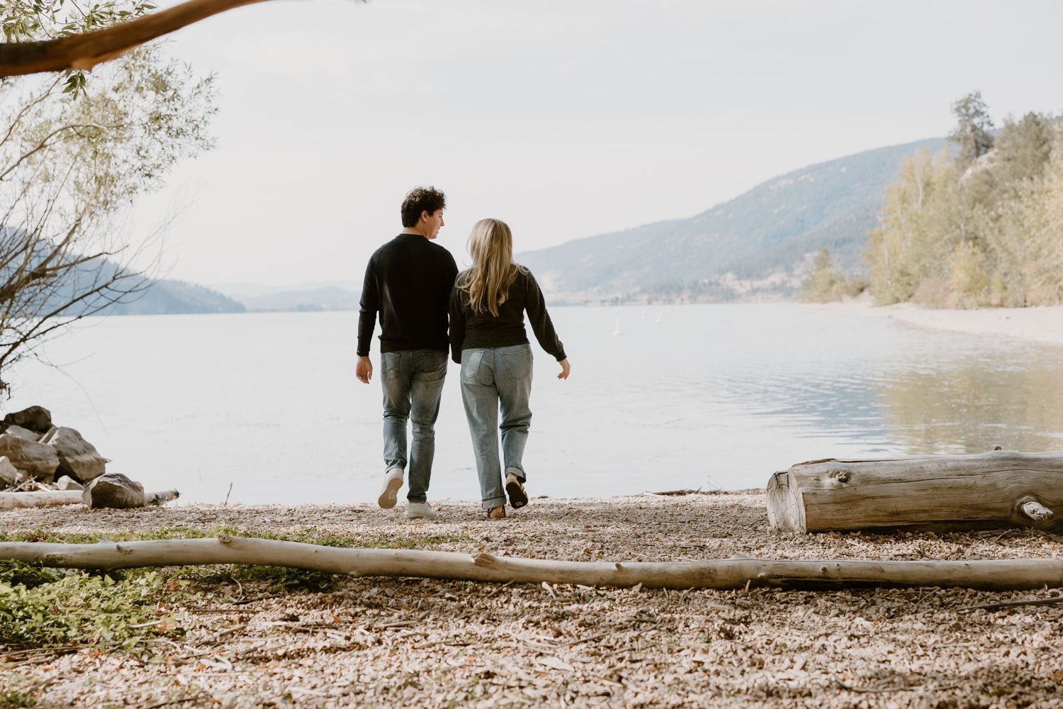 Couple walks along lakeside path with mountains in background.