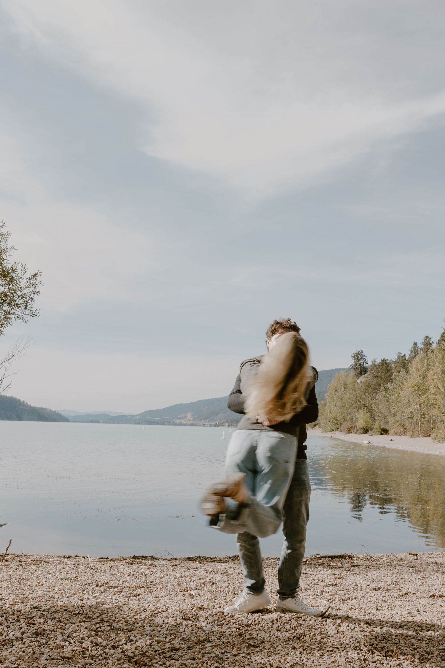 A joyful moment captured as a person jumps playfully on a lakeside beach.