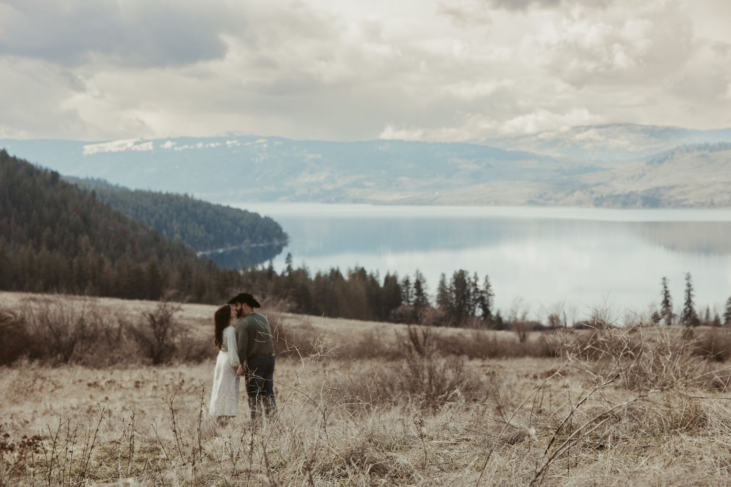 Couple standing on hill overlooking misty mountain lake landscape.