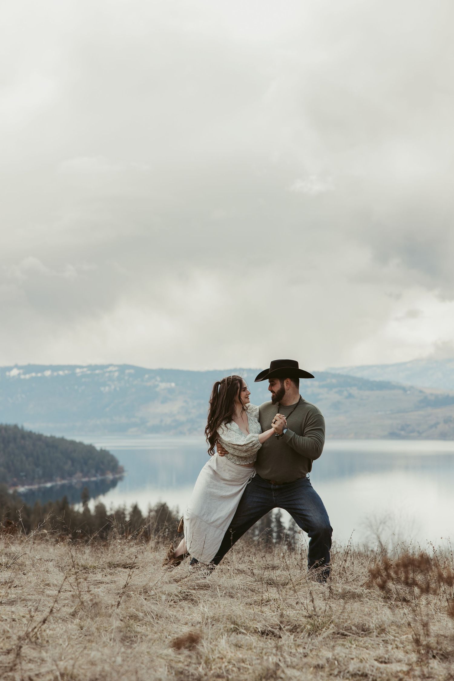 A couple poses dramatically against a scenic mountain lake backdrop in winter.