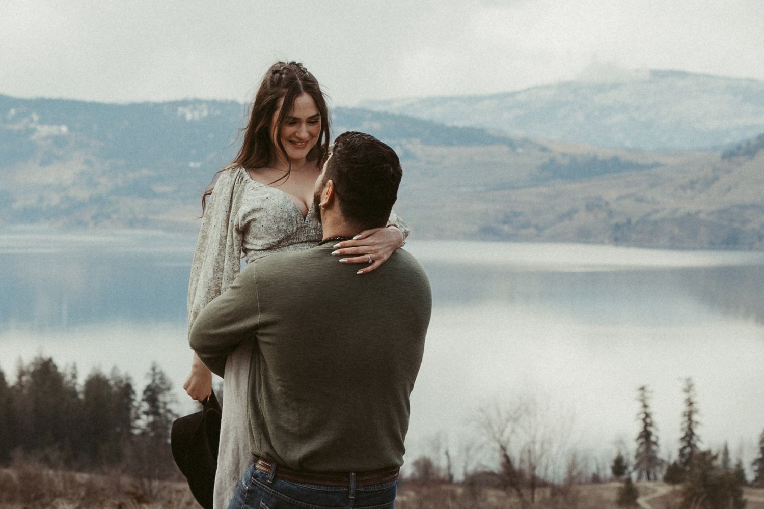 A couple shares an intimate moment overlooking a serene lake landscape.