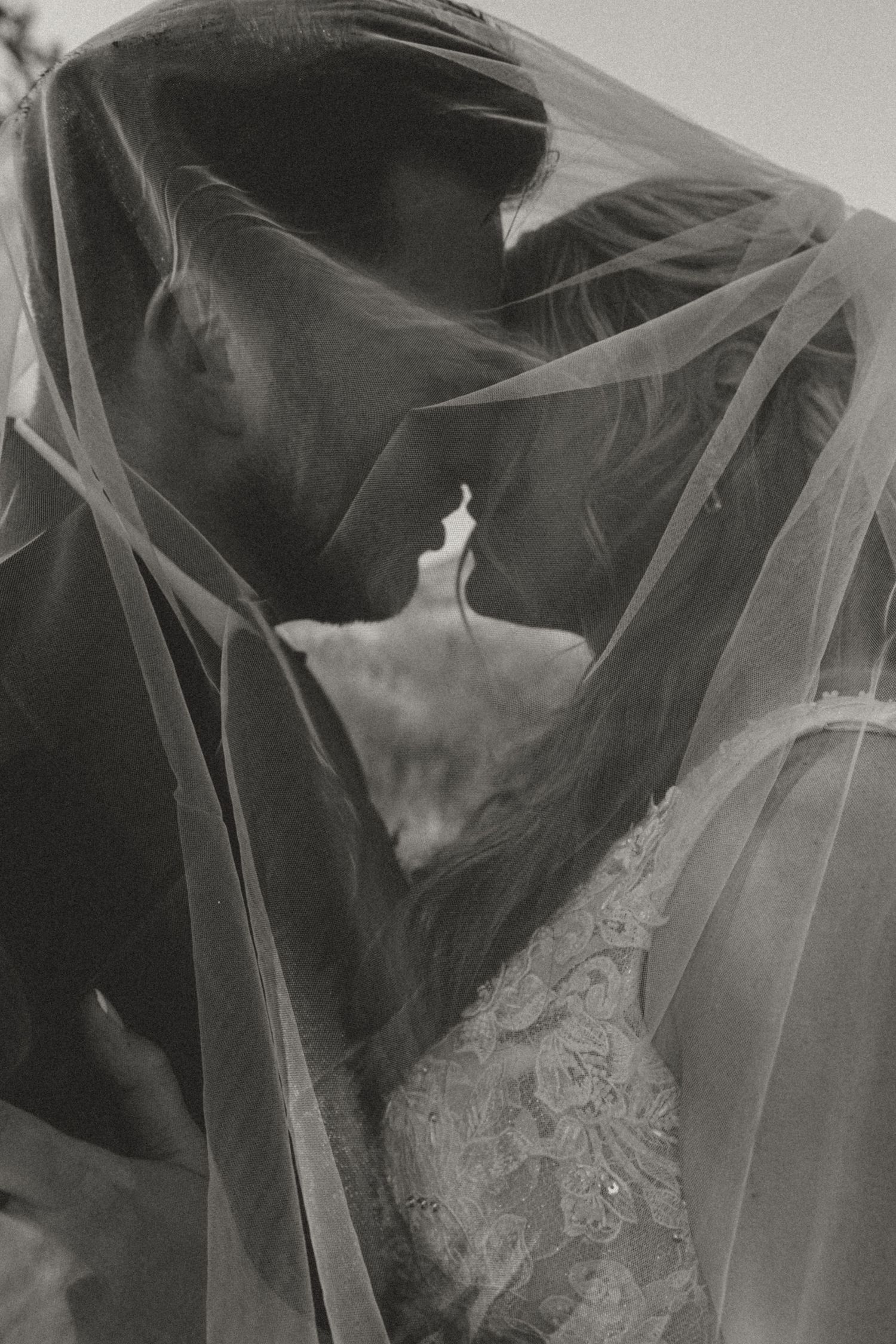 An artistic black and white wedding photo showing a couple under a flowing veil.