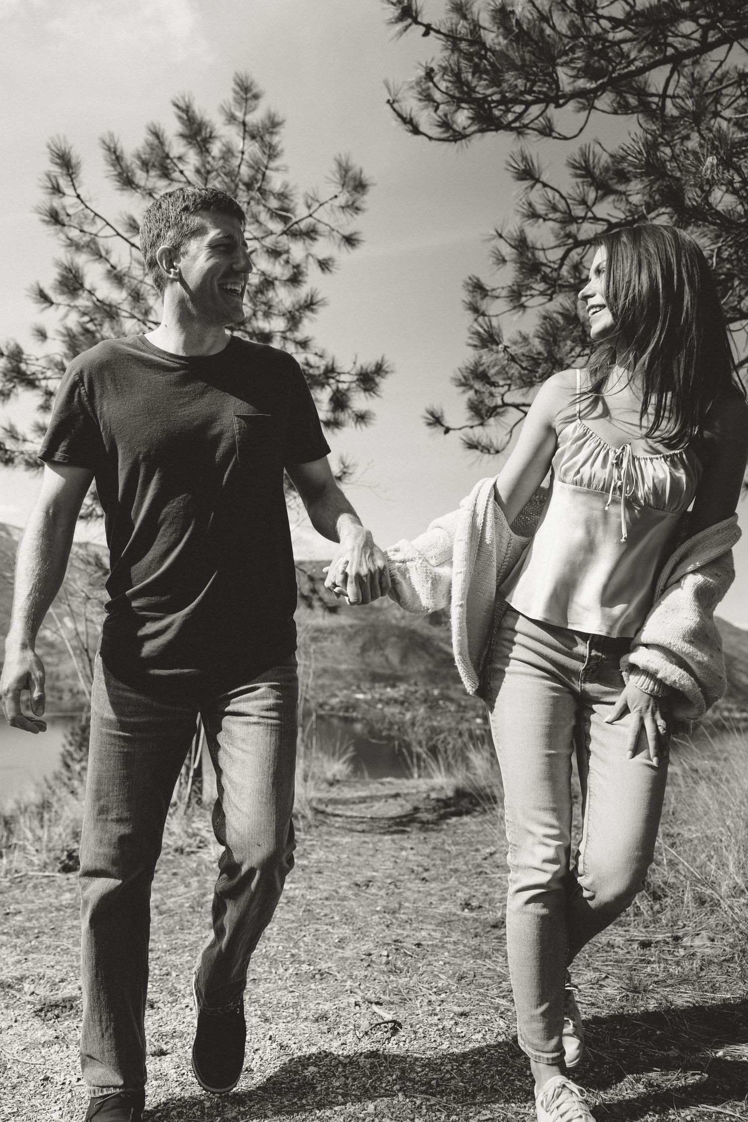 Black and white portrait of couple walking together against pine tree backdrop.