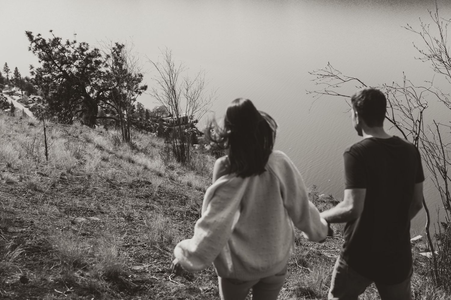Black and white photo of couple walking hand in hand on hillside path.