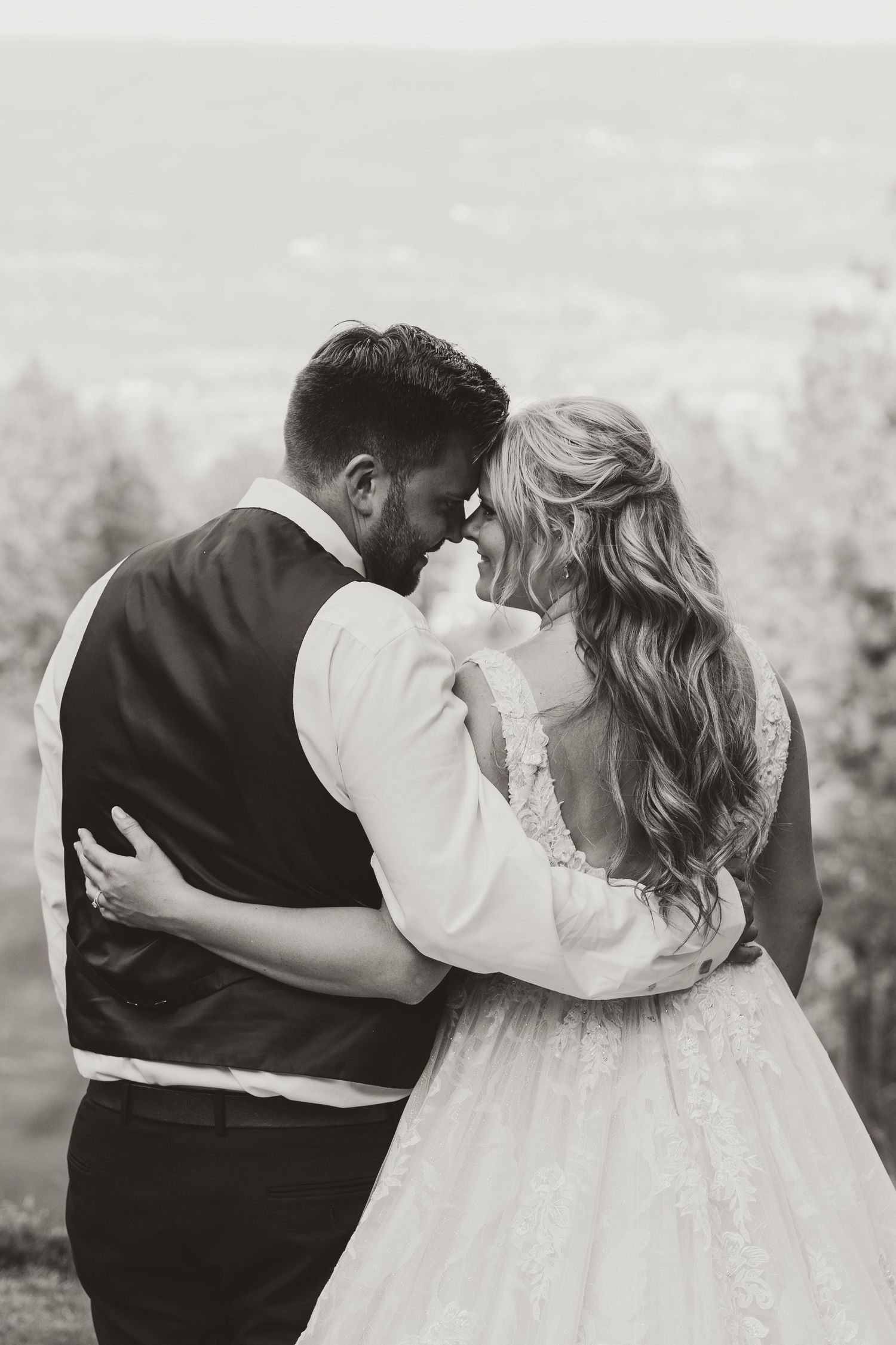 A black and white wedding portrait of a couple embracing against a mountain backdrop.