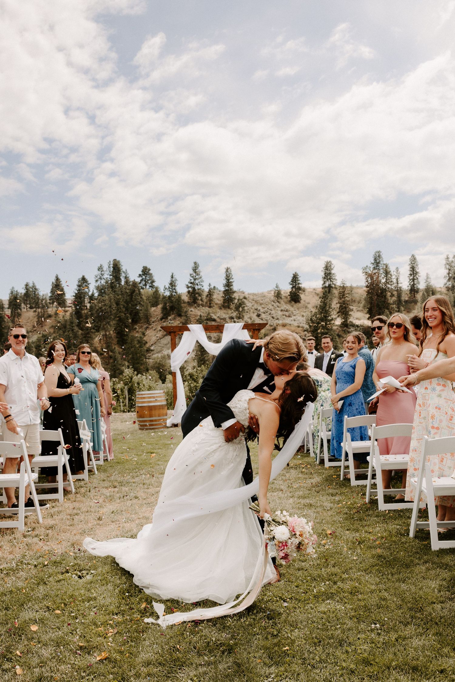 A romantic outdoor wedding ceremony dip in a mountain setting with pine trees and white chairs for guests.