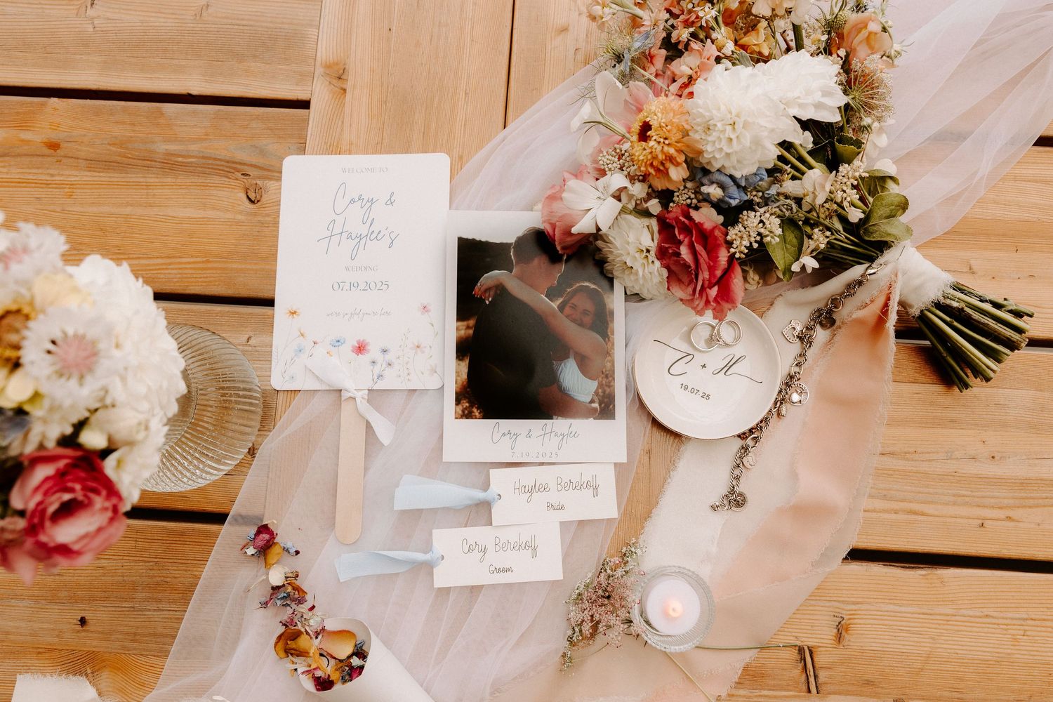 Wedding details with floral bouquet, invitation cards, and polaroid photos laid out on rustic wooden planks.