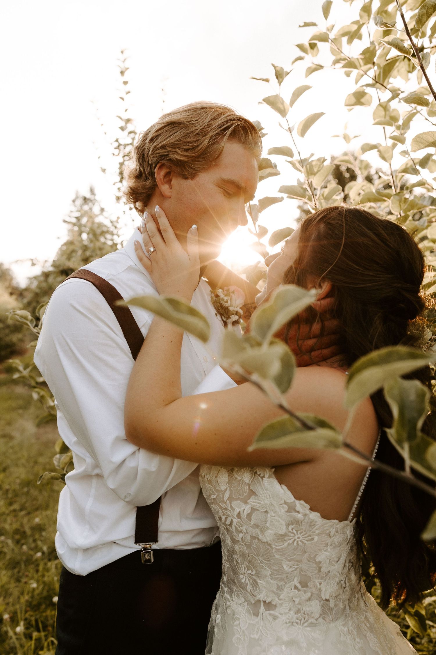 Romantic sunset wedding portrait showing an intimate moment between newlyweds among sunlit foliage.