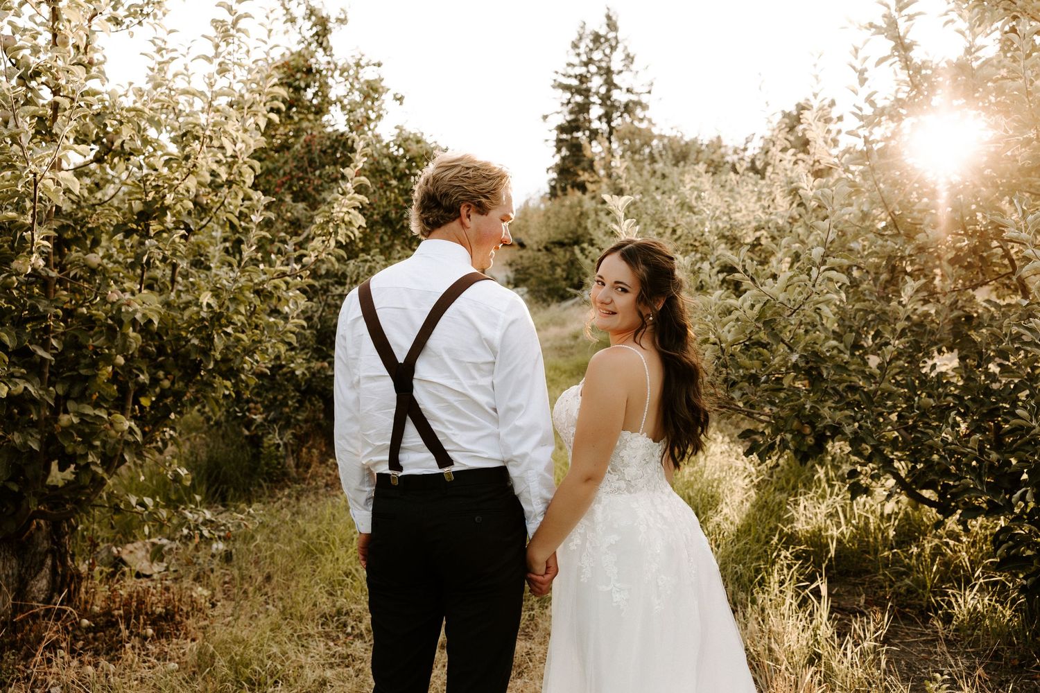 A couple shares a tender moment during sunset in a garden setting with the groom wearing white and suspenders.