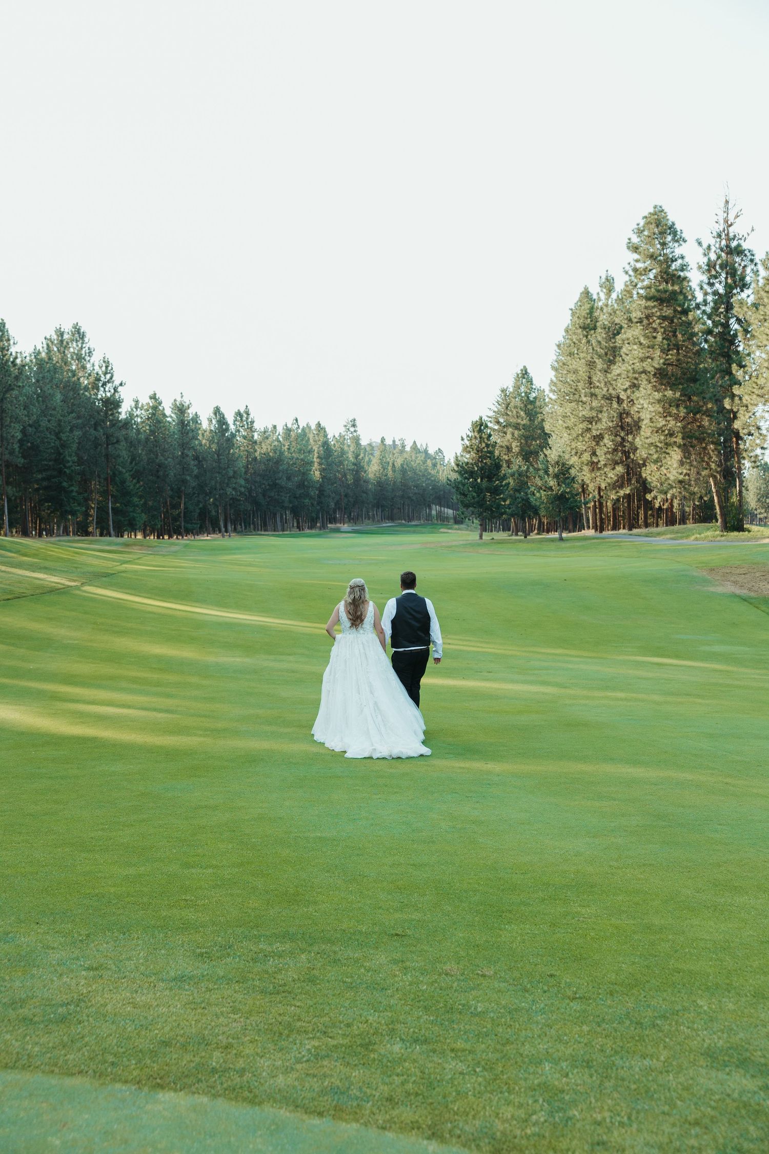 A couple in wedding attire walks across a beautifully manicured golf course.