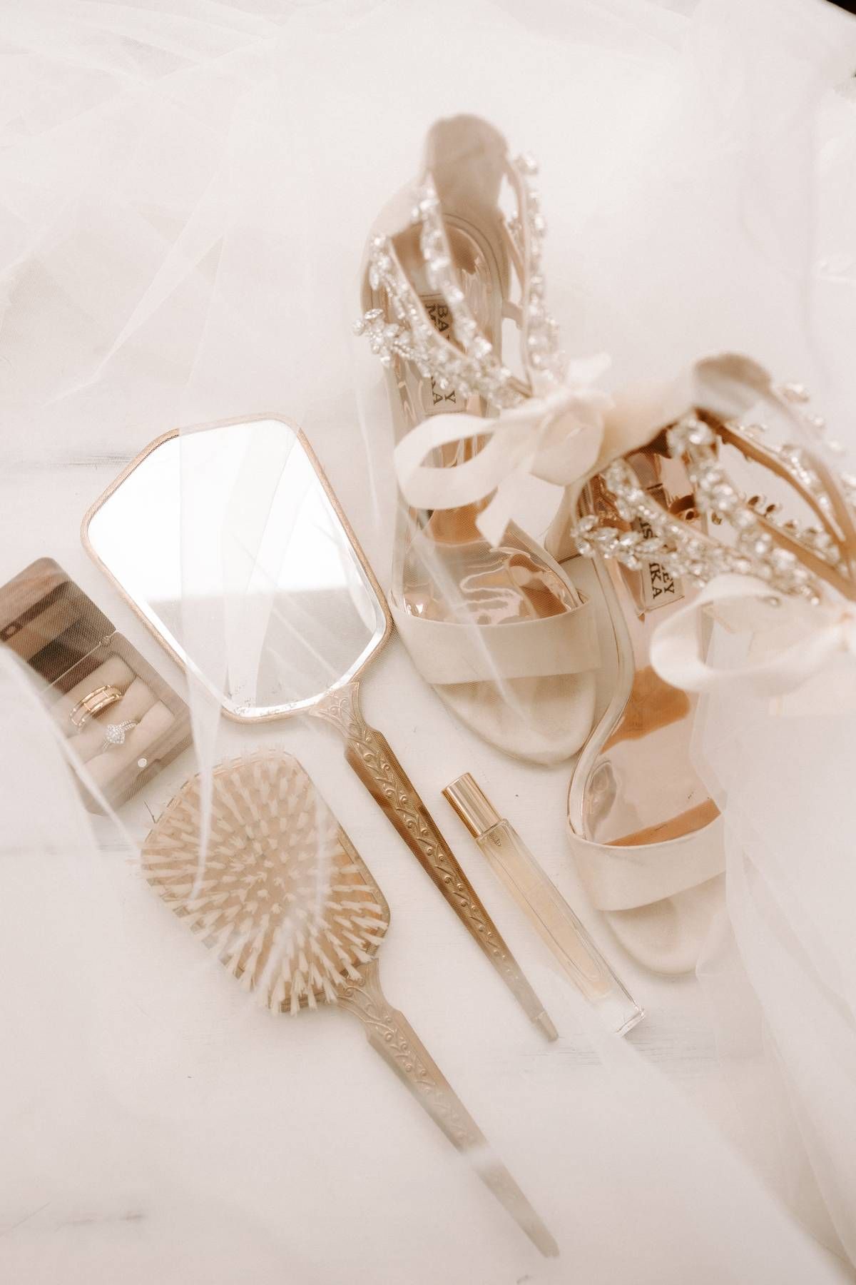 Wedding accessories including white heels, hairbrush, and styling tools arranged on light fabric.