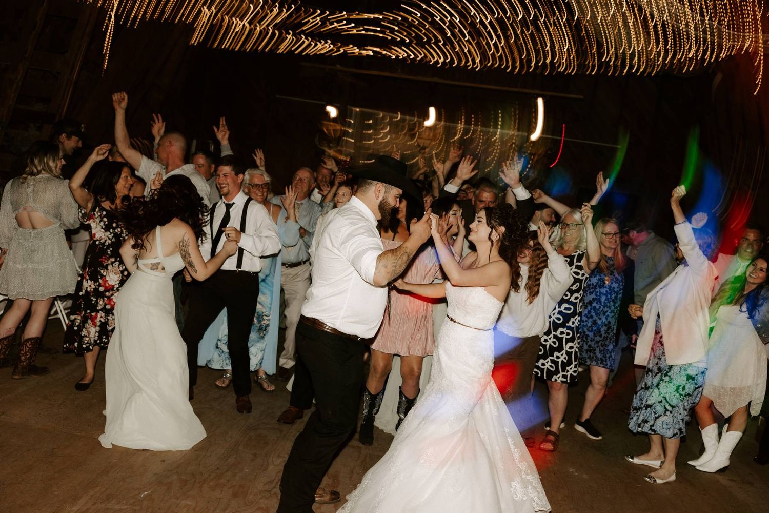 Wedding reception guests dancing together on a crowded dance floor under a rustic thatched roof venue.