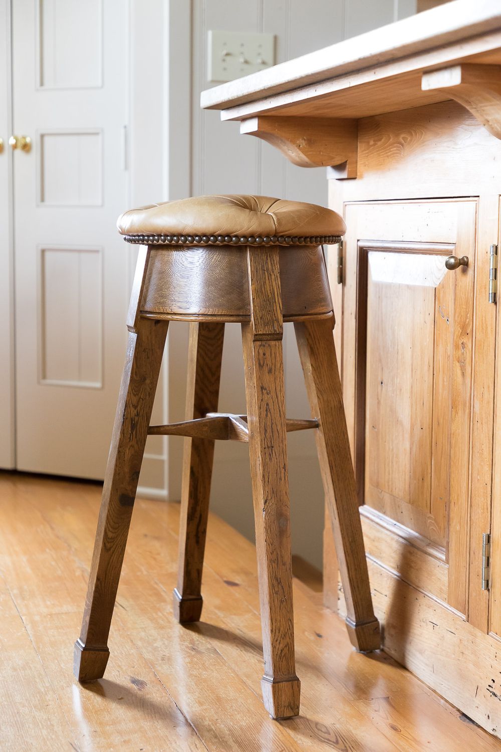 Vintage wooden bar stool with leather cushion seat against kitchen cabinets.