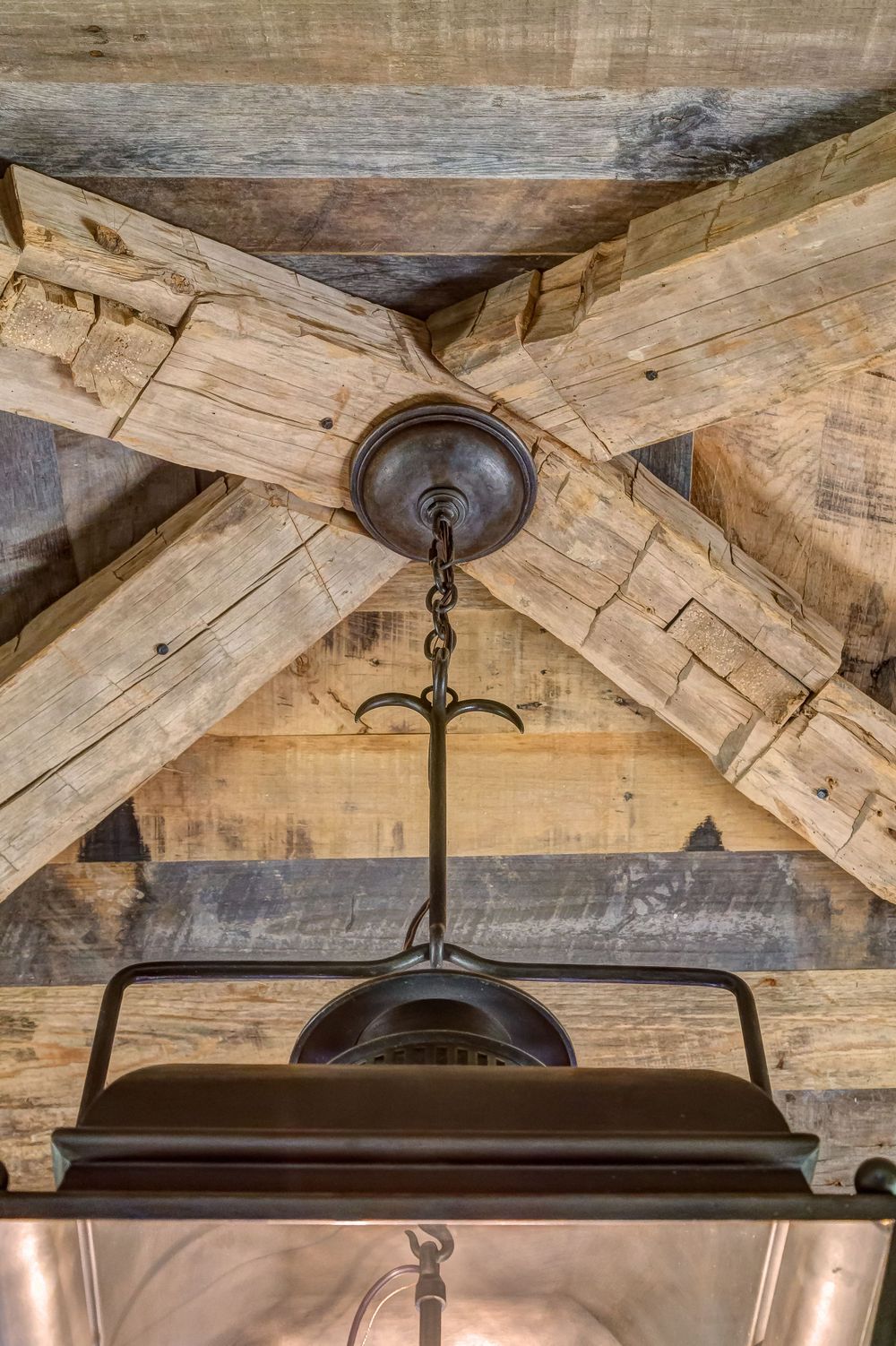 Rustic wooden beam ceiling with vintage pendant light fixture hanging from exposed crossed timbers.
