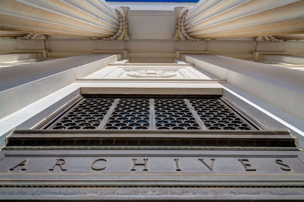 Architectural detail of ornate archival building facade with decorative metalwork grating.