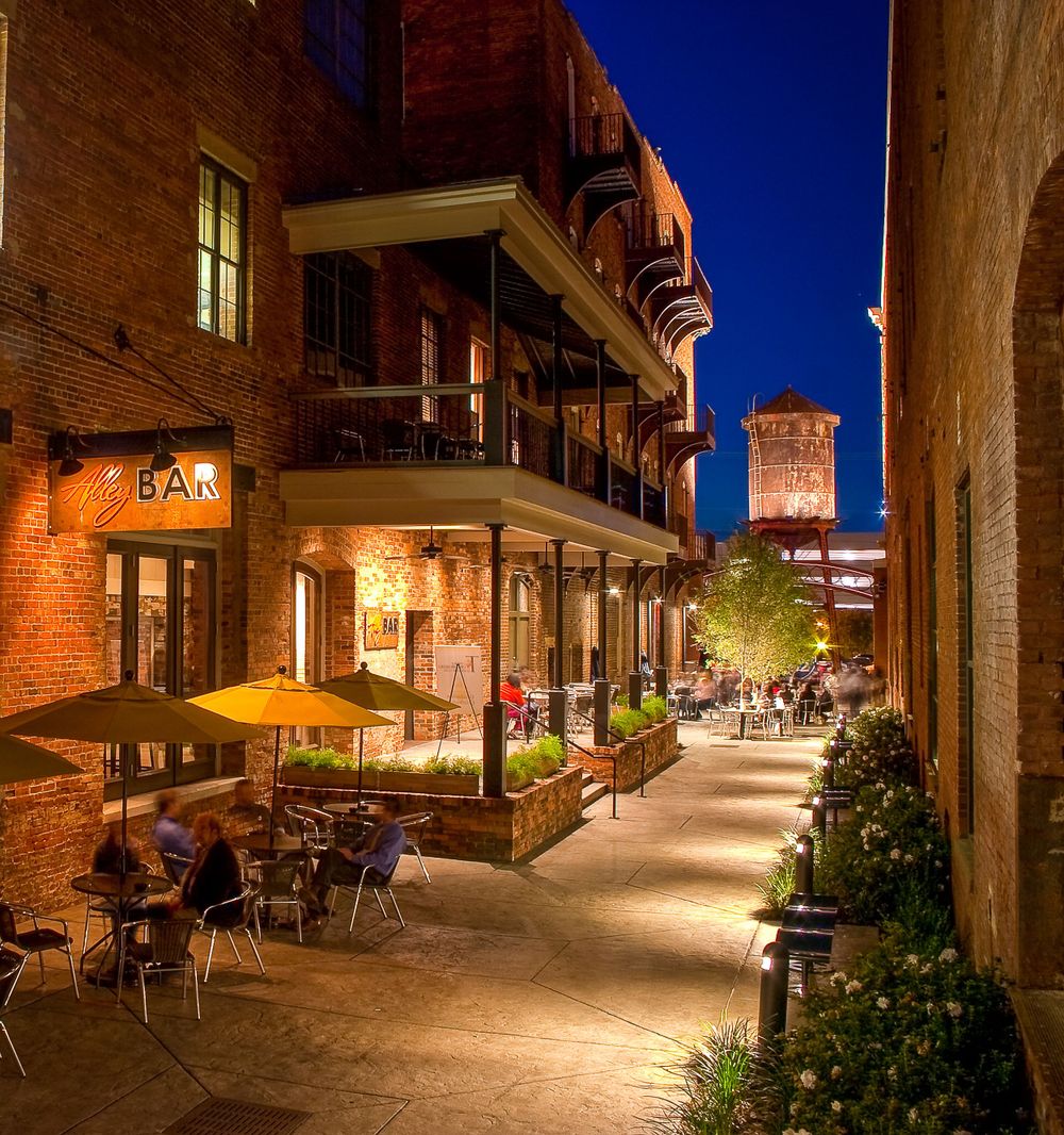 Historic brick buildings with outdoor dining along illuminated street at dusk.