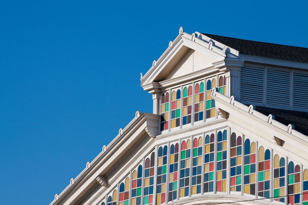 White building facade with geometric pattern of multicolored glass panels beneath classical pediment.