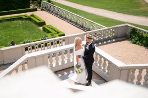 Brud och brudgum delar en romantisk stund på trappsteg med en elegant balustrad av vit sten i en formell trädgård.