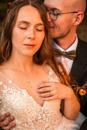 Brudgummen kysser ömt bruden på kinden medan hon sluter ögonen, vilket framhäver hennes skira spetsklänning och guldhalsband.