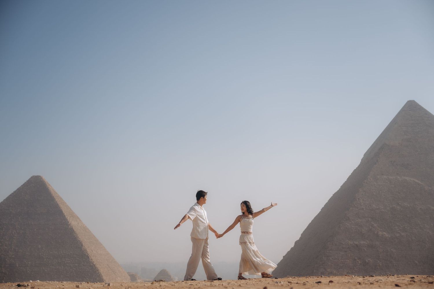 Two decorated camels flank a couple posing in front of the iconic pyramids of Giza in Egypt.