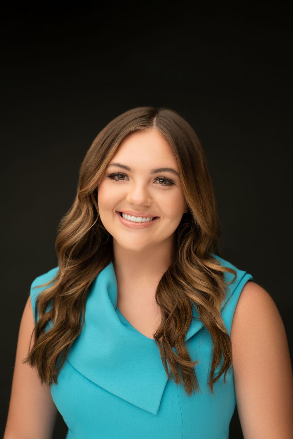 Professional portrait in a turquoise sleeveless top against dark background.