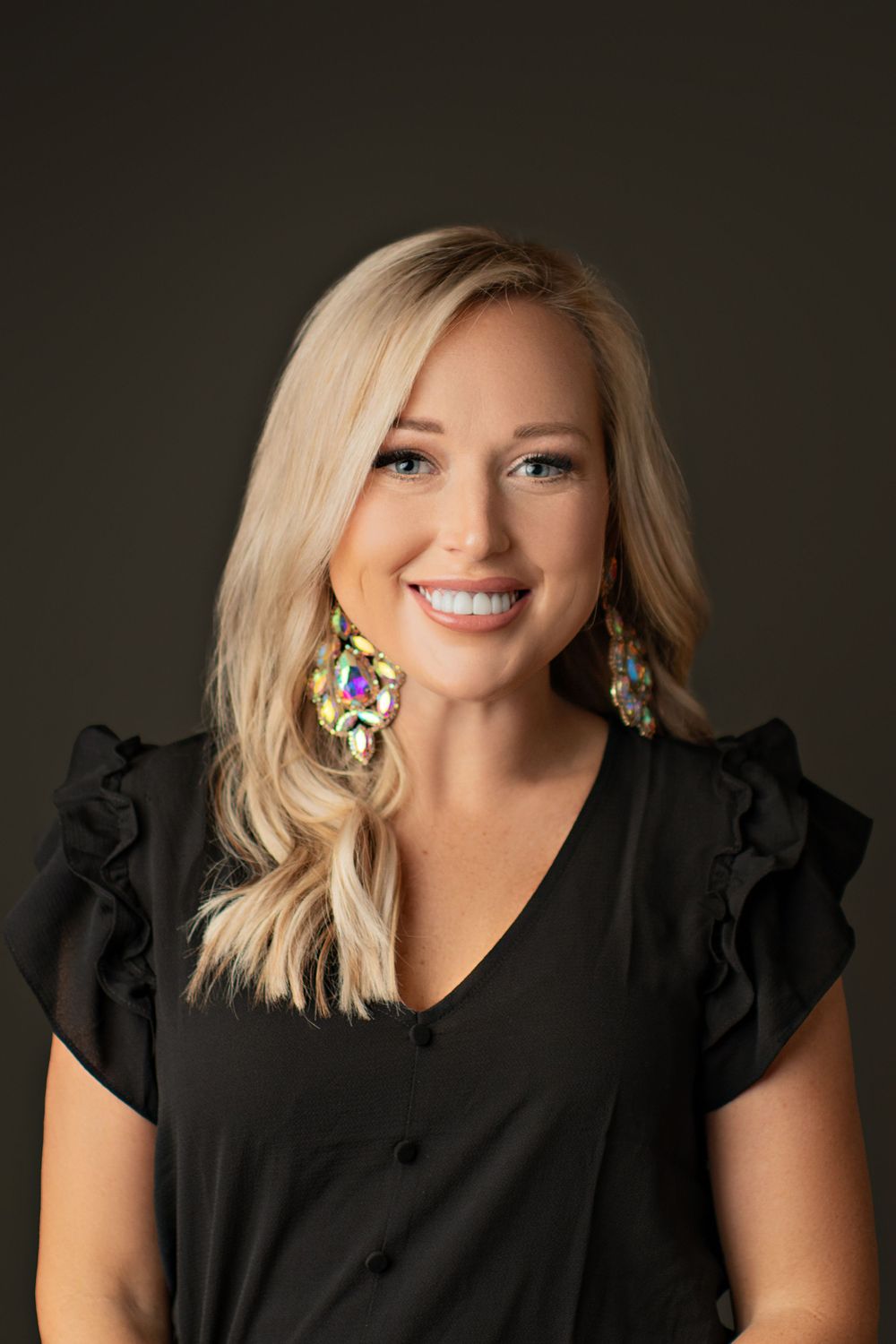 Professional headshot against dark background wearing sparkly statement earrings.