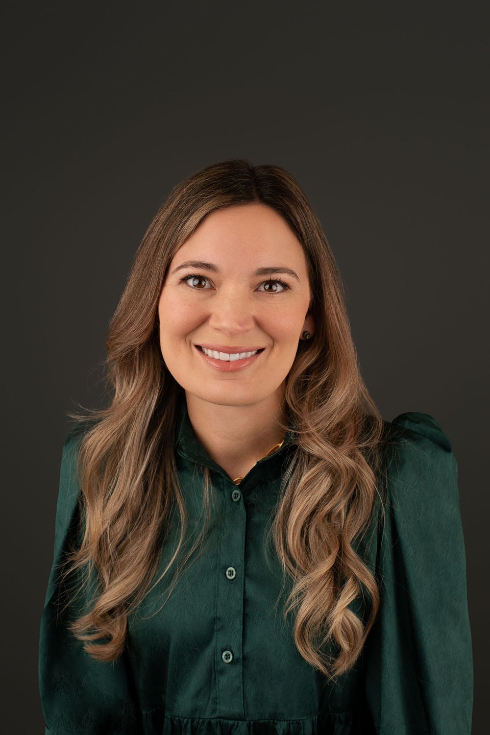 Professional headshot wearing dark green button-up blouse against dark background.