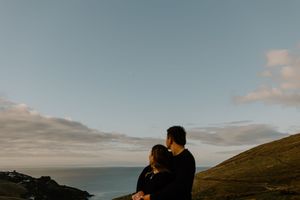 Cinematic coastal landscape shot showing silhouetted figures against a moody sky at sunset.