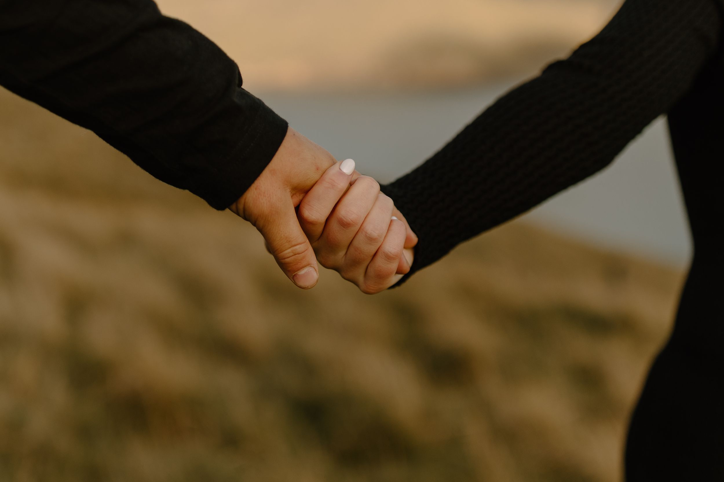 A couple holding hands in a rustic outdoor setting with warm golden sunset lighting and mountains in the background.