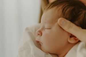 Close-up profile view of peacefully sleeping baby with dark hair against white bedding.