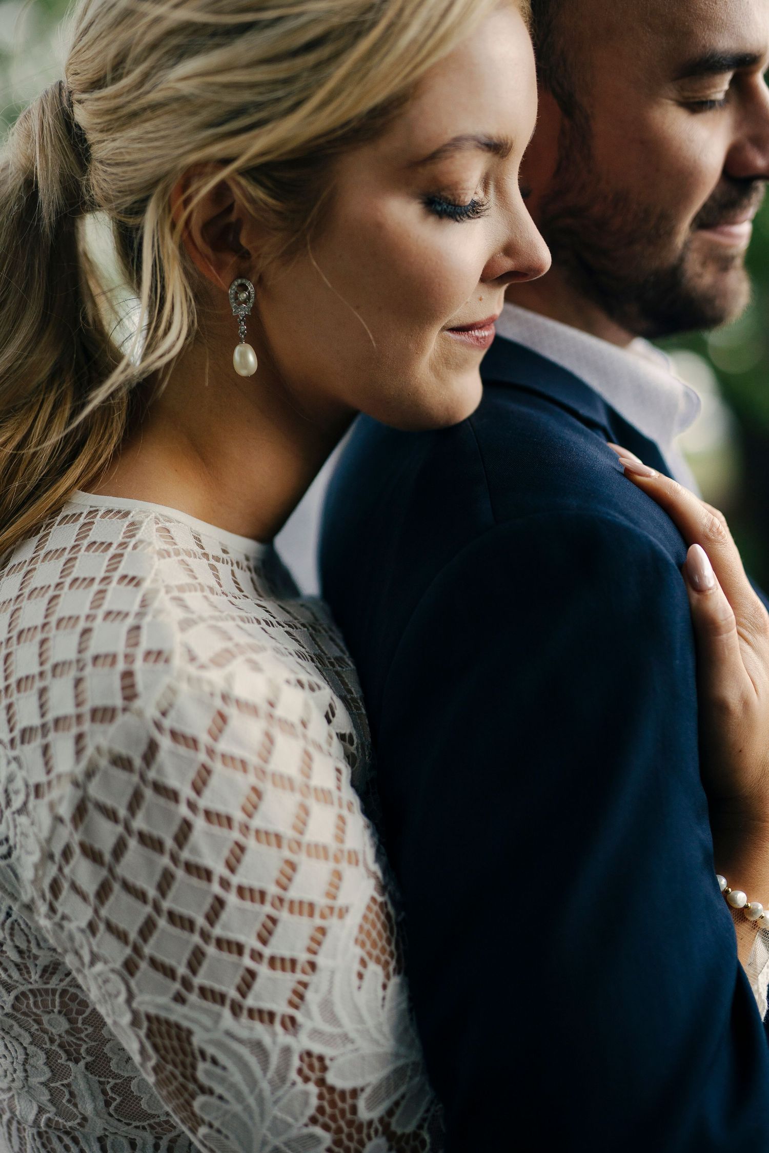 Intimate wedding portrait with lace dress details and tender embrace against dark background.
