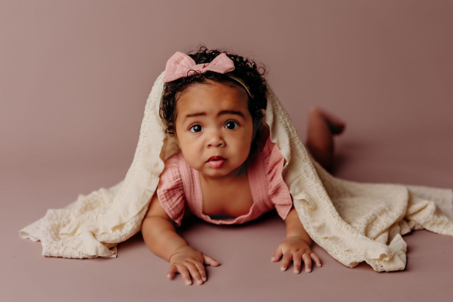 Baby wearing vintage bonnet smiling against pink floral backdrop.