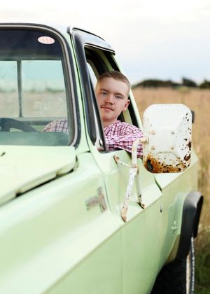Someone poses with a vintage mint green classic car in a rural setting.