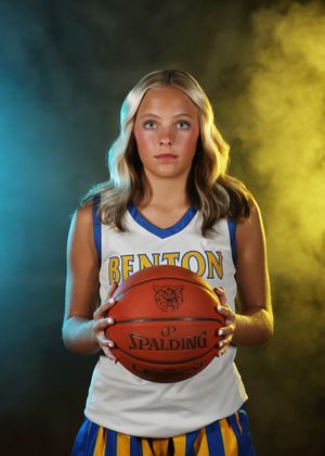 Young female basketball player in Benton jersey holding a Spalding basketball against a dramatic blue and yellow smoke background.