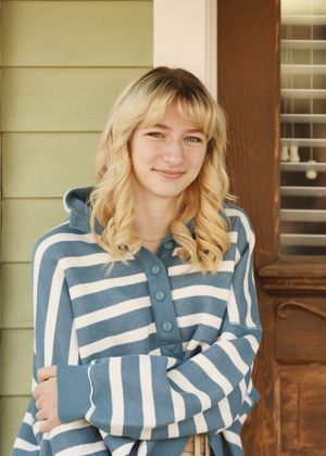 A portrait of someone wearing a blue and white striped sweater against a wooden door and green siding.