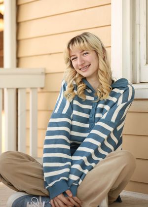 A casual portrait on a porch wearing a cozy striped sweater and khaki pants.