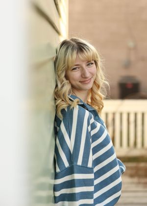 A casual portrait against a wall wearing a blue and white striped sweater with wavy hair.