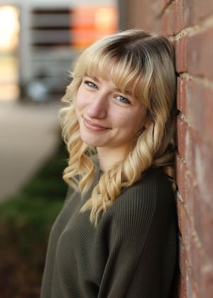 A warm portrait against red brick wearing an olive sweater with soft natural lighting.
