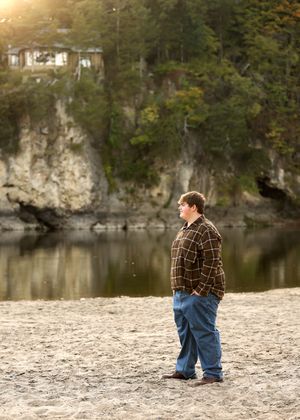 Someone in plaid and jeans stands on a rocky shoreline near limestone cliffs.
