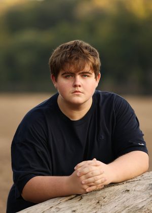 Portrait of someone in a navy t-shirt leaning against a rock during golden hour.