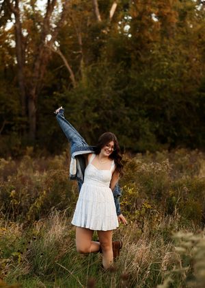 Someone in a white dress twirling with a denim jacket in a field at sunset.